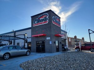 Front picture of Club Car Wash with cars parked to the left and cars lined up to go into the wash on the right.