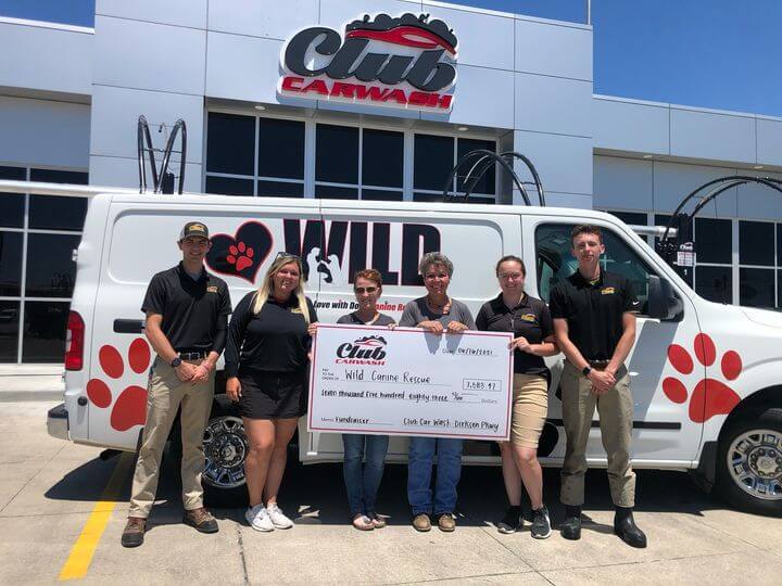 group of club car wash representatives with wild canine representatives holding check in front of wild canine vehicle