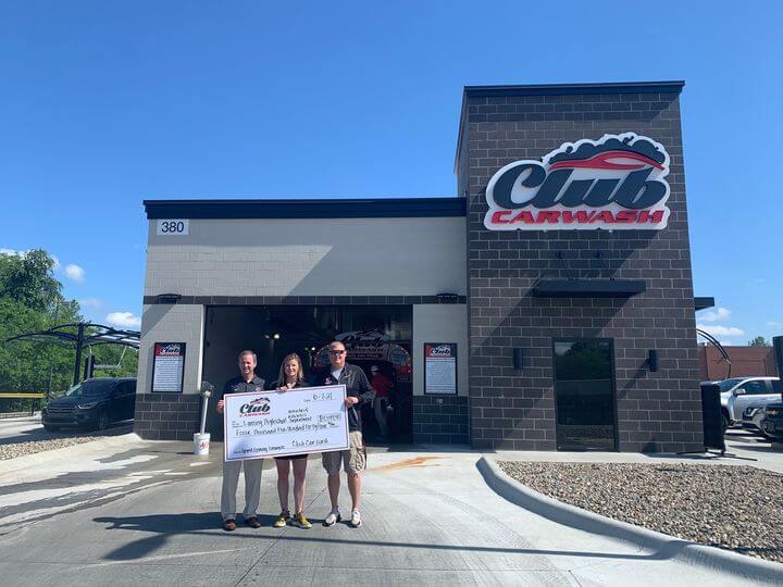 car wash employees and lansing high school representative holding big check in front of club car wash