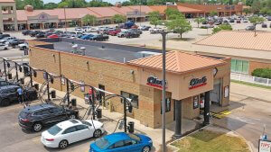renovated tan building with parking lot on the left and shopping center in parking lot at top with club car wash logo building entry way