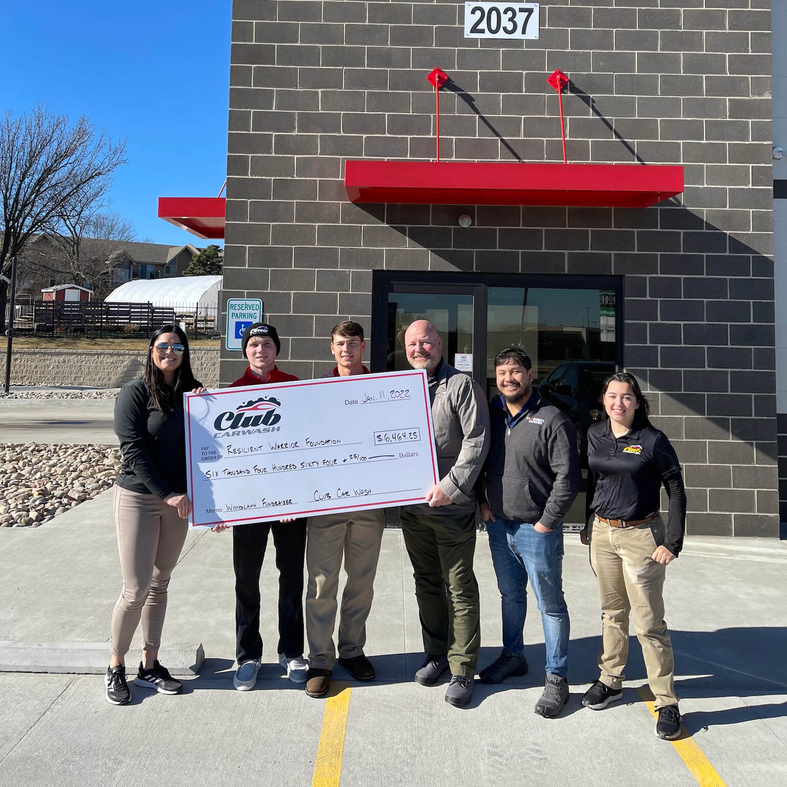 Group of Club Car Wash employees with Resilient Warrior representatives holding a large check in front of the car wash.